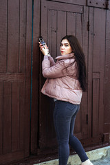 Fototapeta premium Young cute pregnant girl in pink warm down jacket trying to open the key lock. Late autumn, the cold is coming. toned photo. Very big door