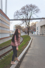 A young cute pregnant girl in a pink warm down jacket is trying to walk on a high curb. Late autumn, the cold is coming.