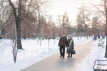 Fototapeta na wymiar Romantic senior couple walking in the park in winter time. Love forever. Background of white winter snow