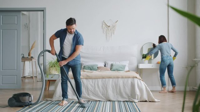 Man and woman are busy with housework in bedroom cleaning room with vacuum cleaner and duster caring for hygiene and tudiness. People and housekeeping concept.