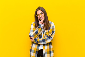 young  pretty woman looking happy and smiling with hand on chin, wondering or asking a question,...