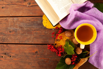 Cropped photo of a white cup with tea and a violet sweater strewn with orange maple leaves on a wooden table. The concept of comfort, coziness and hygiene. Autumn mood, fall season. Selective focus,