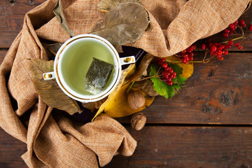 Cup of tea near a scarf making makeup, top view. A cup of green tea near beautiful yellow leaves. Hot drink on wooden background. Autumn concept of beauty and drinks. autumn.