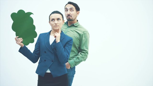 A young business woman standing on a white background. Thinks of a man in a green shirt. Holds a green speech bubble in his hands. Slow video.