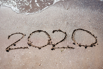 2020 written in beach sand and washed by a wave