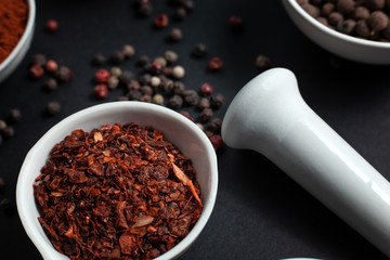 Paprika spice in a ceramic bowl next to peas scattered with peppercornsand caraway seeds in a ceramic mortar on a black background