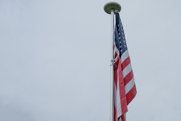 USA flag on a flagpole with gray sky, with space
