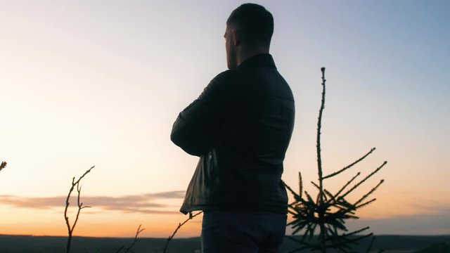 Man stands on top and looks at the sunset with different clouds in the sky. Close up slow motion epic footage. 4k.