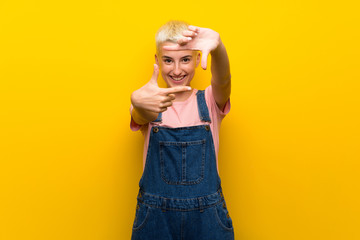 Teenager girl with overalls on yellow background focusing face. Framing symbol