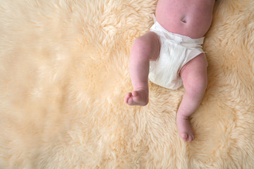 Newborn baby legs with white nappy, diaper on a fur background.