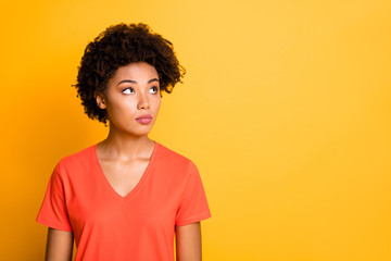 Obraz na płótnie Canvas Photo of pretty dark skin lady looking empty space without smiling wear orange v neck t-shirt isolated yellow color background