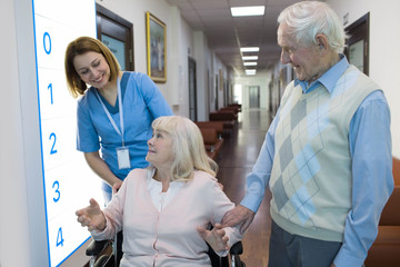 Obraz premium senior woman in wheelchair talking with nurse in a hospital behind her standing senior husband.