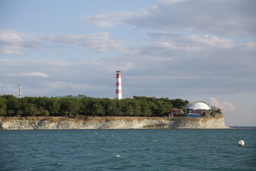 lighthouse on coast of sea. White and red color lighthouse. Against the blue sky. View from the sea.
