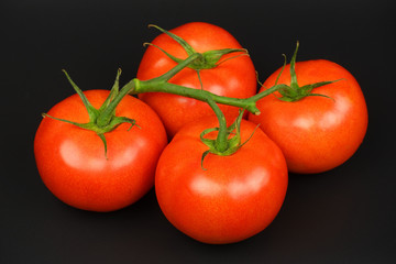 Four fresh juicy red bunch tomatoes on black background top view