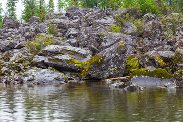 Stony shore of the lake with a creek on the Teletskoye lake in the Altai mountains with coniferous trees and a creek during the rain in the fall. Loneliness, travel, calm, bad weather.