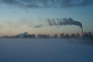 Fototapeta premium Sunset on a very cold winter day, with a smoking chimney.