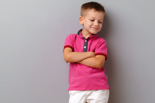 Cute little boy in pink T-shirt posing against grey background