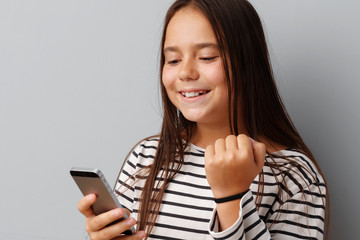 Fototapeta premium Happy casual little girl looking at her phone over gray background