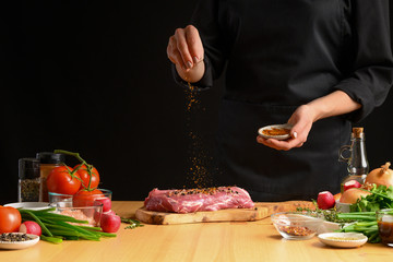 Pork steak and seasoning from the chef in the background. Horizontal photo. With vegetables, tomatoes, hot peppers, onions and a chapel. With black background