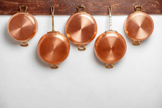 Row of shiny clean copper pans, different size, hung on wooden plank