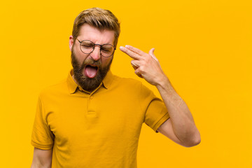 young blonde man looking unhappy and stressed, suicide gesture making gun sign with hand, pointing...