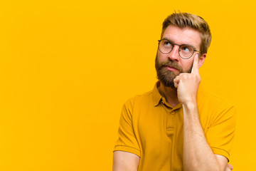 young blonde man with a concentrated look, wondering with a doubtful expression, looking up and to...