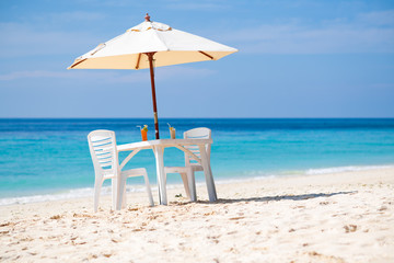 Private white beach chairs and umbrella setup with cocktails for couple on white sand beach next to the beautiful Andaman sea of Phuket, Thailand.
