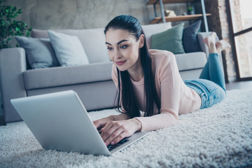 Close up photo of pretty lady chatting with friends over notebook reading new email letter lying comfy on floor wearing pullover and jeans in apartment
