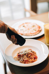 Close up of woman hand holds wooden oak pepper mill grinder over the dish of spaghetti in white plate in Italian restaurant.