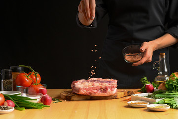 Chef cooks pork ribs. sprinkling with salt on a background with vegetables. Freezing in motion. Recipe book, cooking, restaurant business