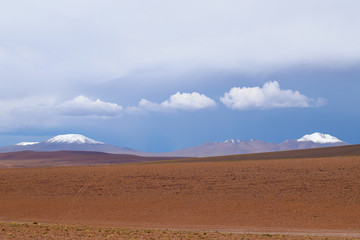 Fototapeta na wymiar Landscape of the Bolivian highlands. Desert landscape of the Andean plateau of Bolivia with the peaks of the snow-capped volcanoes of the Andes