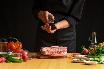 Chef cooks pork ribs. sprinkling with pepper on a background with vegetables. Freezing in motion. Recipe book, cooking, restaurant business