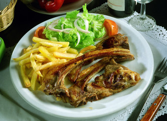 Plato de costillas de cordero con patatas fritas y ensalada.