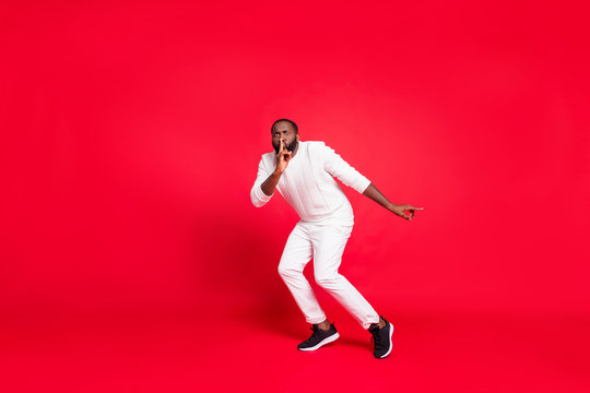 Full size photo of funny dark skin man making newyear surprise for girlfriend going tiptoe hold finger on lips wear knitted sweater trousers isolated red background