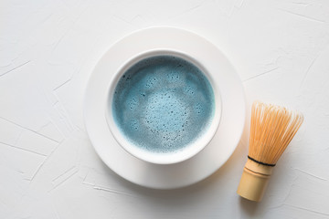 Ceremony blue matcha tea and bamboo whisk on white concrete table. Top view.