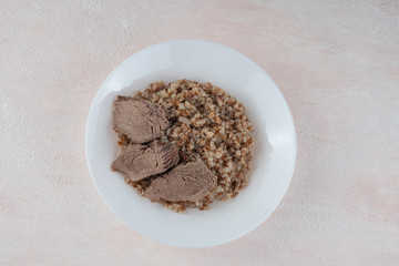 Buckwheat porridge with three pieces of boiled beef on a white plate, light background.