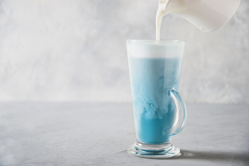 Blue matcha tea and milk in latte glass on grey table. Space for text.