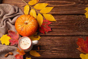 Pumpkin spiced latte or coffee in glass decorated knitted scarf on vintage background. Autum