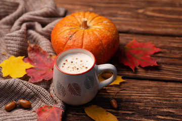 Pumpkin spiced latte or coffee in glass decorated knitted scarf on vintage background. Autum