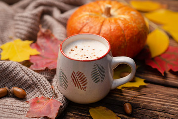 Pumpkin spiced latte or coffee in glass decorated knitted scarf on vintage background. Autum