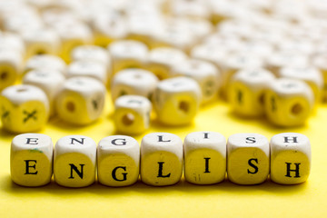 Word english made with block wood letters next to a pile of other letter over wooden table.