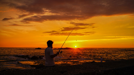 新潟県佐渡島夕陽の中で釣りをする男性