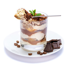 Classic tiramisu dessert in a glass cup on the plate and pieces of chocolate on white background with clipping path
