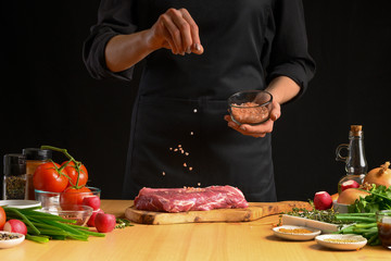 Chef salts steak grill pan. Preparing fresh beef or pork. Horizontal photo with a dark black background.