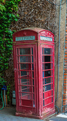Fototapeta na wymiar Abandoned Old Red Phone Booth Against Ivy Covered Wall