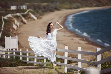 A beautiful girl, bride, in a white dress, barefoot, playing, waving a dress near a white fence, on...