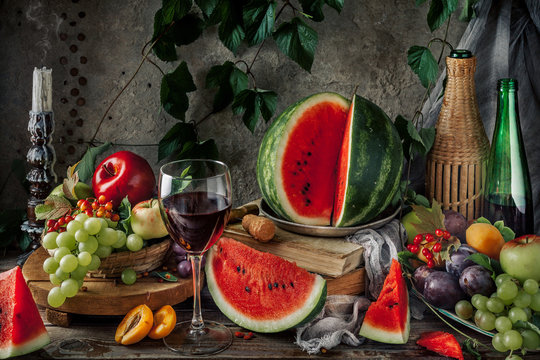 Classic still life with fruit and a glass of red wine. Fruits on a concrete dark background with a vine. rustic style. The concept of rural life.