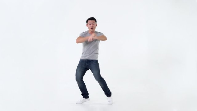 Playful Asian man  dancing happily in many body gestures isolated on light gray background