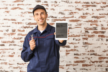 Male car mechanic with tablet computer near brick wall