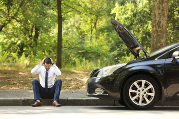 Stressed businessman sitting near broken car outdoors